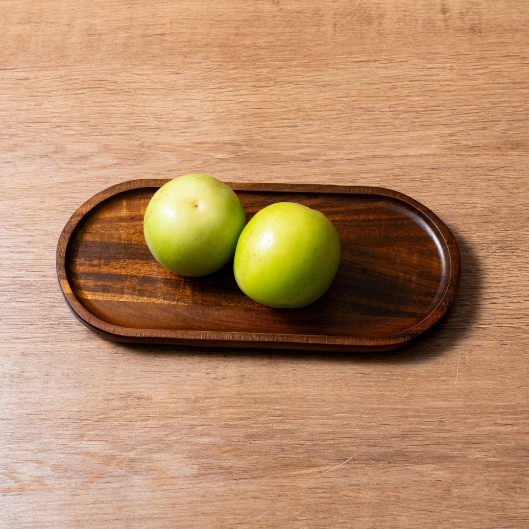 Organic acacia wood tray with two green apples on a wooden surface.