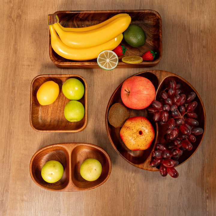 Organic wooden dinner plates with fresh fruits including bananas, apples, grapes, and citrus on a wooden table.