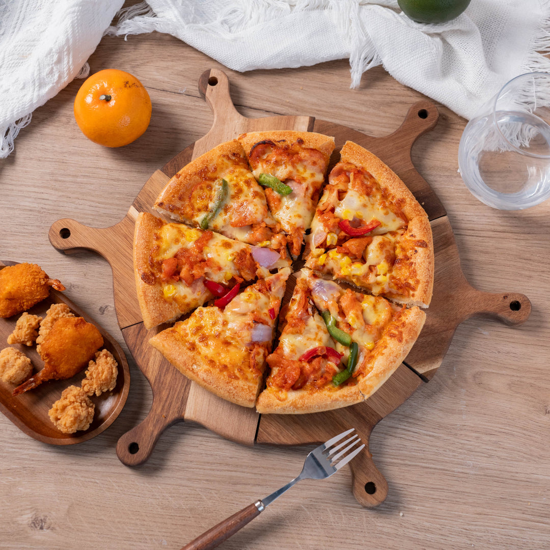 Acacia wood pizza serving tray with sliced pizza, surrounded by appetizers and a glass of water, ideal for sharing meals.
