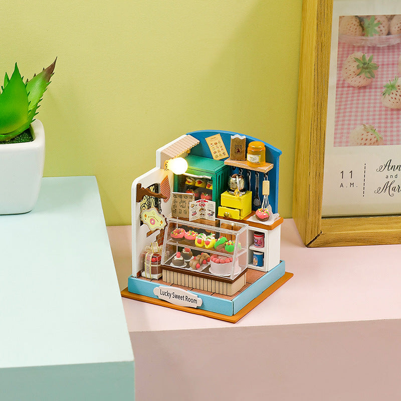 Mini DIY wooden dollhouse kit featuring a colorful sweet shop with various desserts and light decoration.