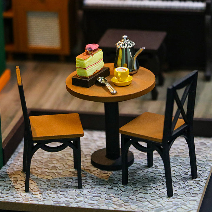 Miniature dining setup with a table, two chairs, a cake, a teapot, and a cup in a DIY dollhouse.