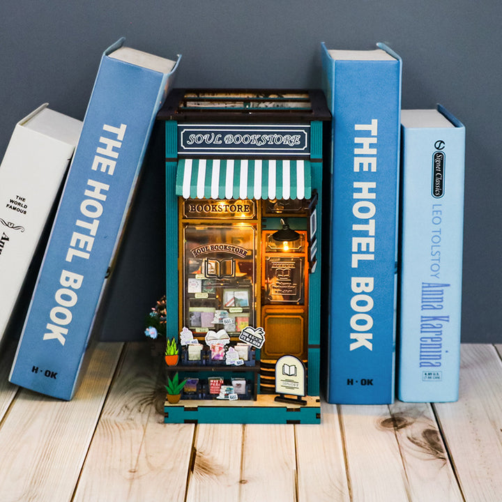 Soul Book Store DIY Book Nook Kit displayed between large books, showcasing its intricate wooden design and musical theme.