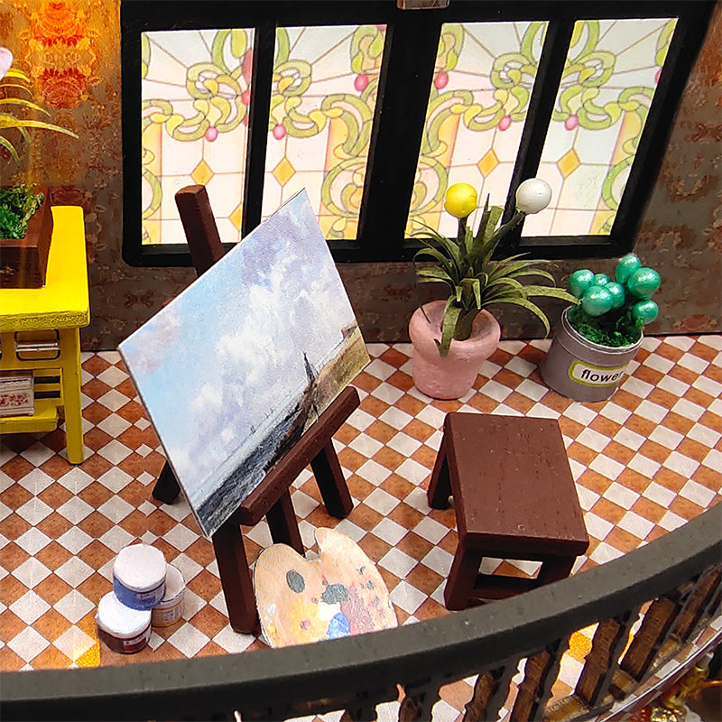 Miniature art studio in dollhouse with easel, potted plants, and colorful decor elements.