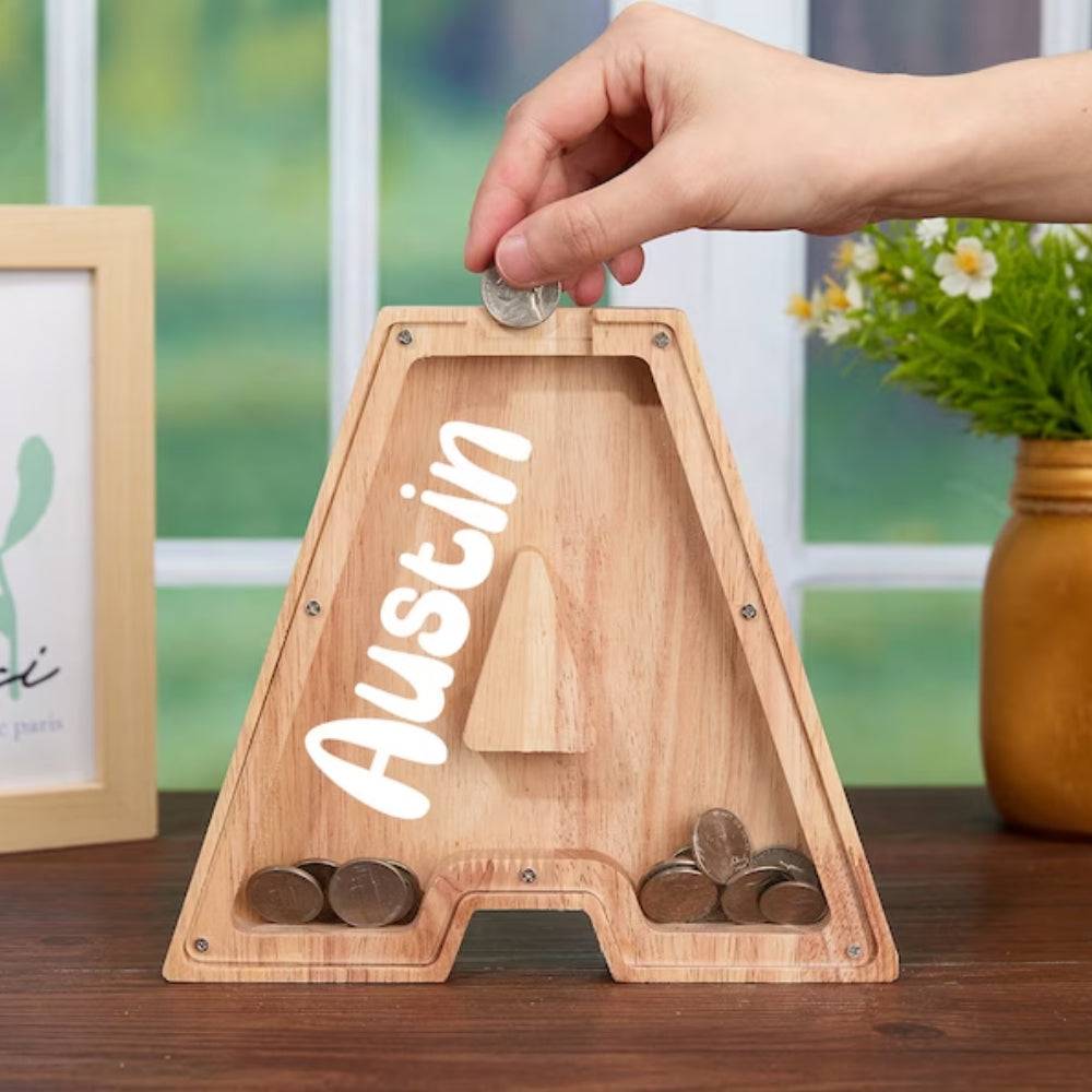 Personalized wooden letter piggy bank with coins, perfect for teaching kids about saving money.