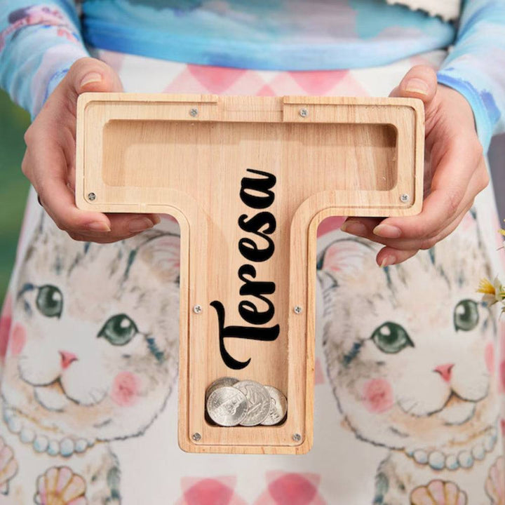 Personalized wooden letter T piggy bank held by a person, showcasing savings coins, ideal gift for kids.