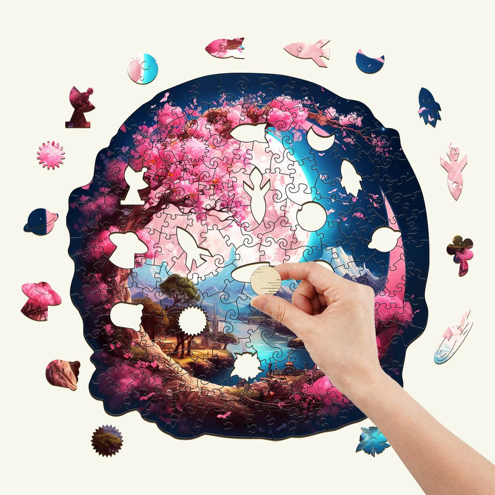 Hand placing a piece in a beautiful moon wooden jigsaw puzzle featuring a serene garden scene with pink cherry blossoms.