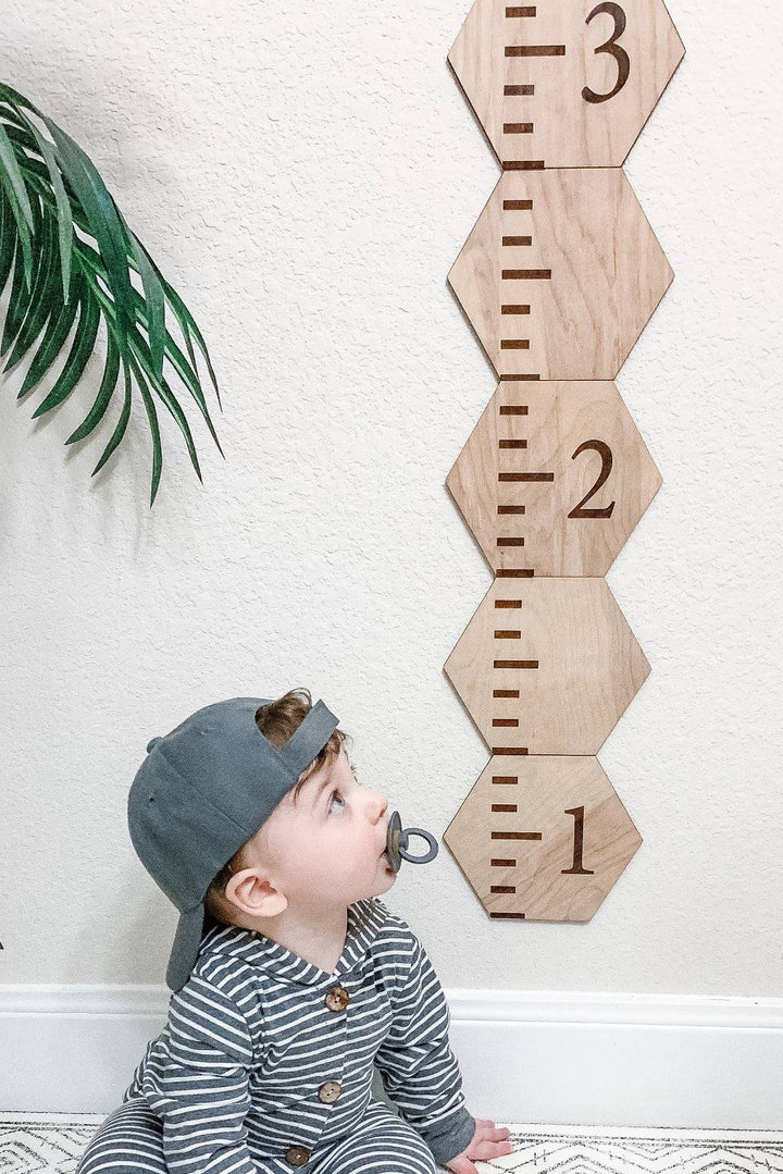 Child gazing at a personalized wooden hexagon growth chart with clear height markings on the wall.