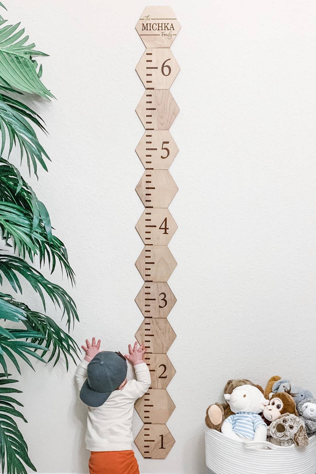 Personalized wooden hexagon growth chart for kids with clear height markings, featuring a child reaching for it.