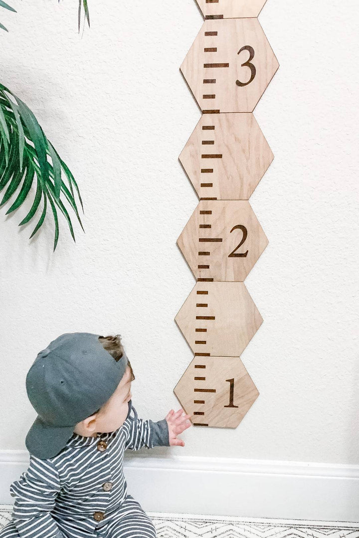 Child interacting with personalized wooden hexagon growth chart, featuring engraved height markers.