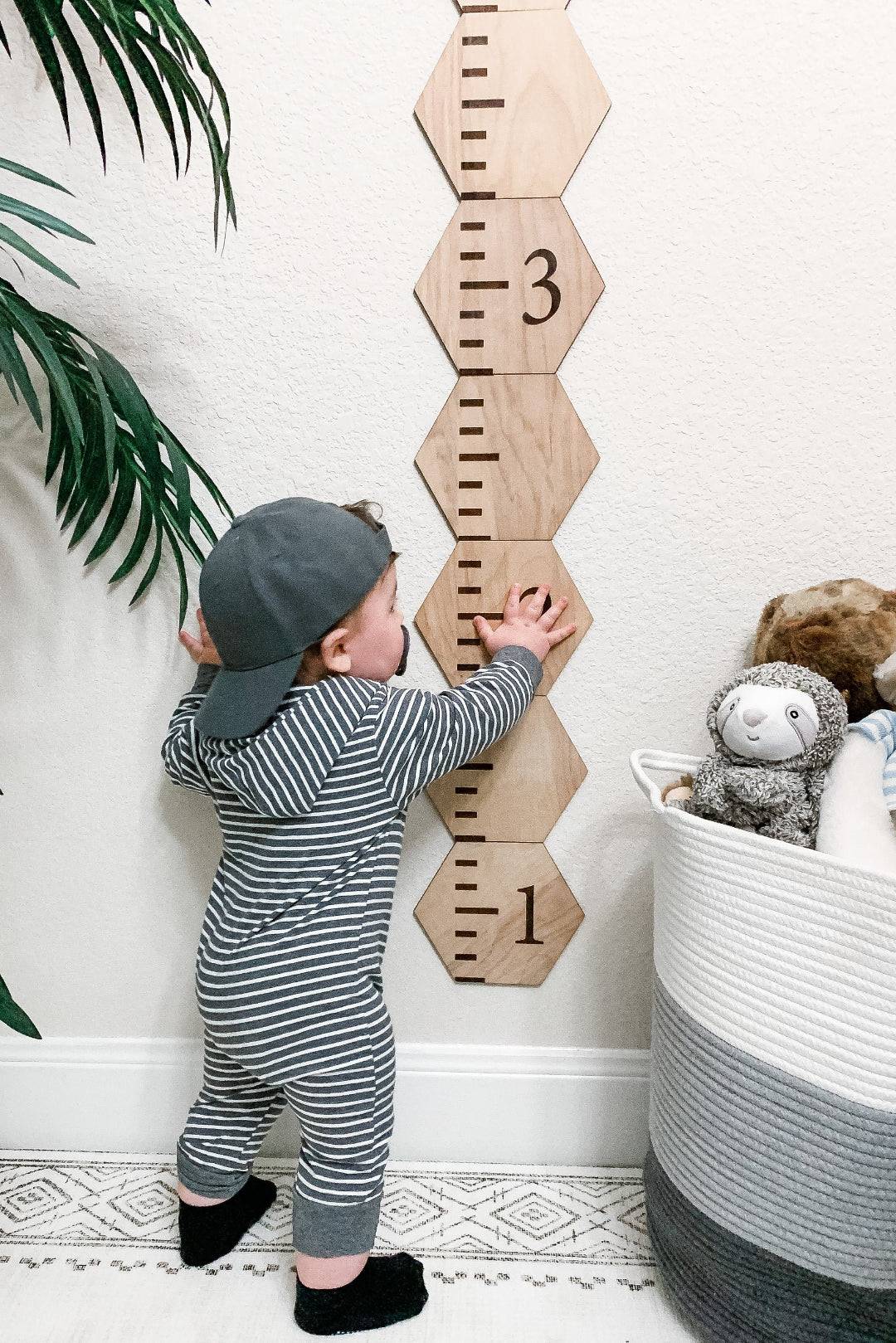Toddler measuring height on a personalized wooden hexagon growth chart against a wall.