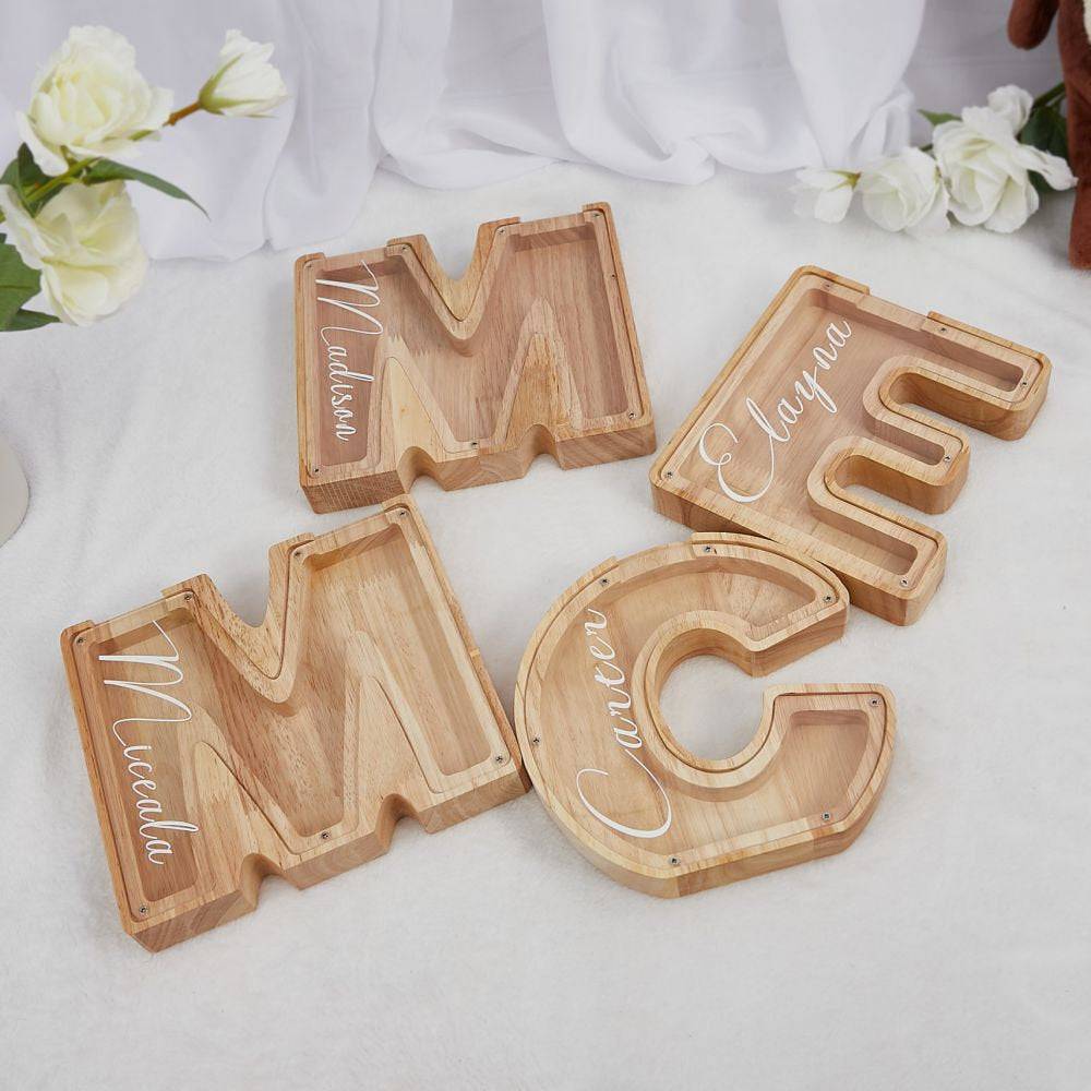 Personalized wooden letter piggy banks for kids displayed on a table with floral decorations.