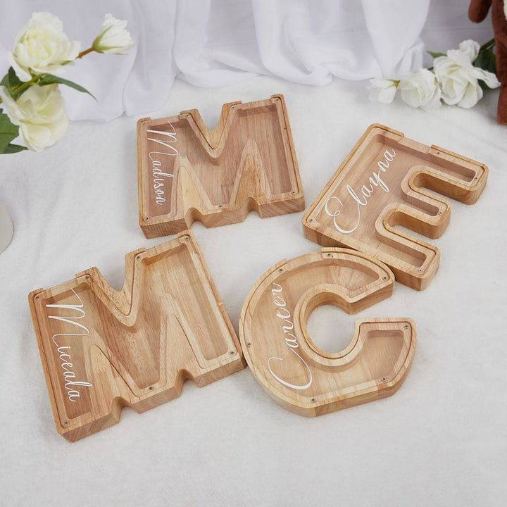 Personalized wooden letter piggy banks for kids displayed on a table with floral decorations.