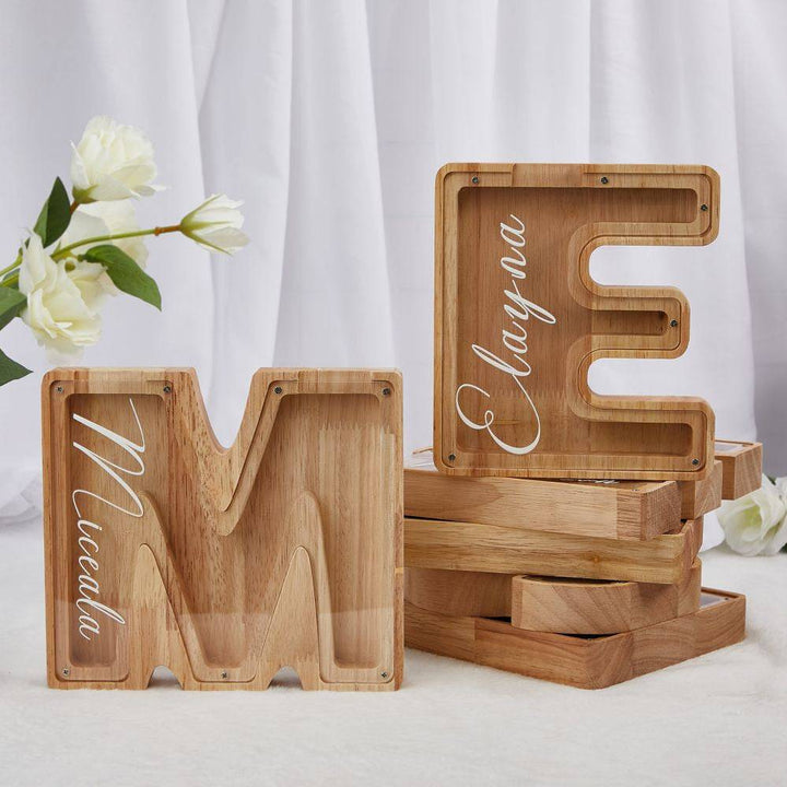 Personalized wooden letter piggy bank with names Miceada and Elayna, designed for children's savings.