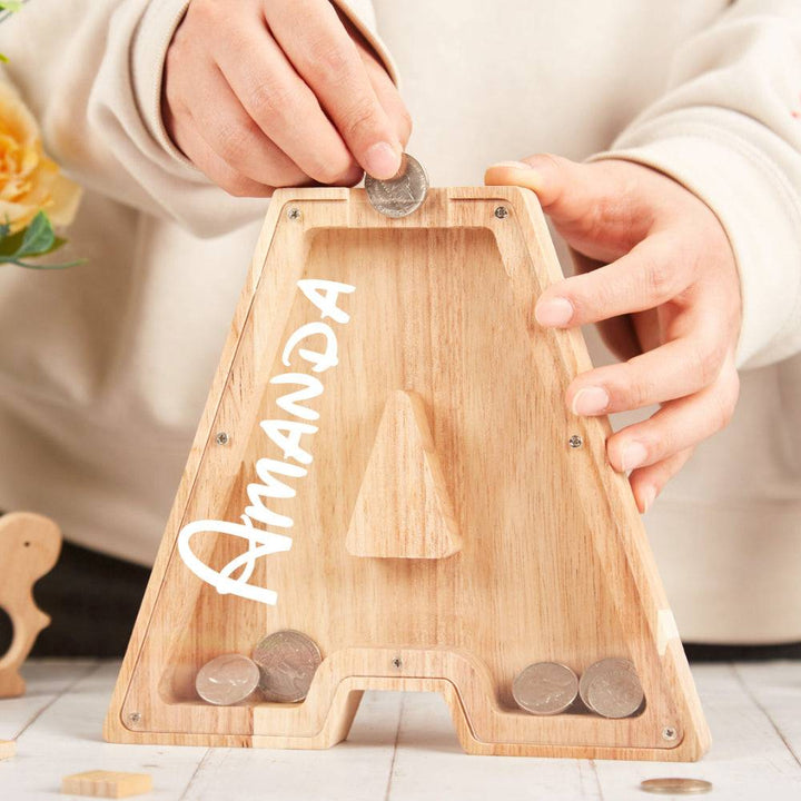 Child inserting coins into a personalized wooden letter piggy bank named Amanda, promoting savings awareness.