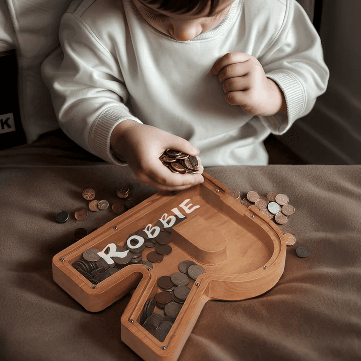 Child with wooden letter piggy bank named Robbie, counting coins, teaching savings lessons.