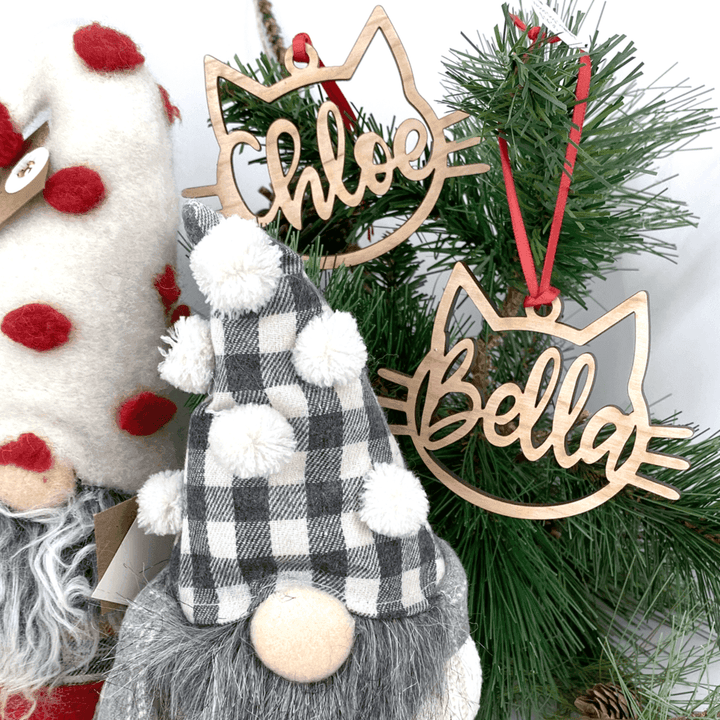 Personalized wooden cat ornaments 'Chloe' and 'Bella' hanging on a Christmas tree with decorative gnome.