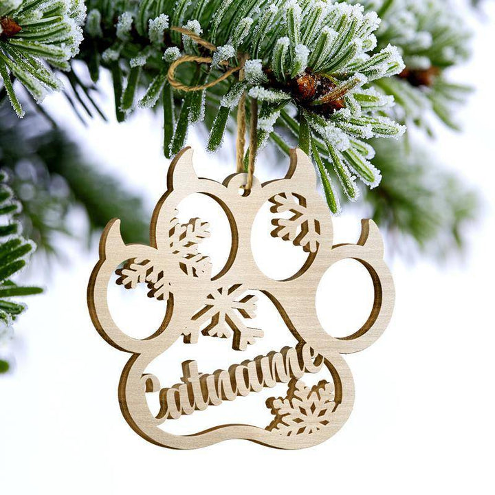 Personalized cat paw wooden ornament with angel wings hanging on a frosted pine branch, festive holiday decoration.