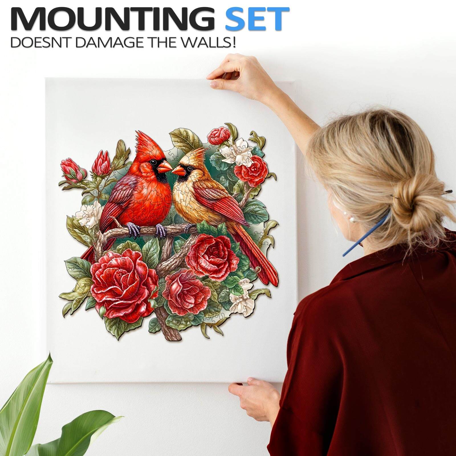 Woman hanging a vibrant cardinal jigsaw puzzle with floral designs using a wall-safe mounting set.