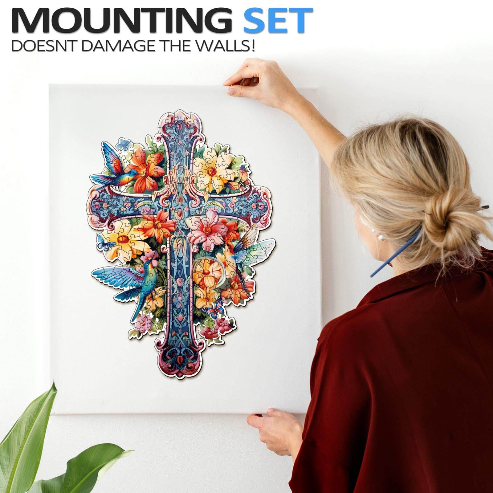 Person mounting a colorful floral cross artwork on a wall using a damage-free mounting set.