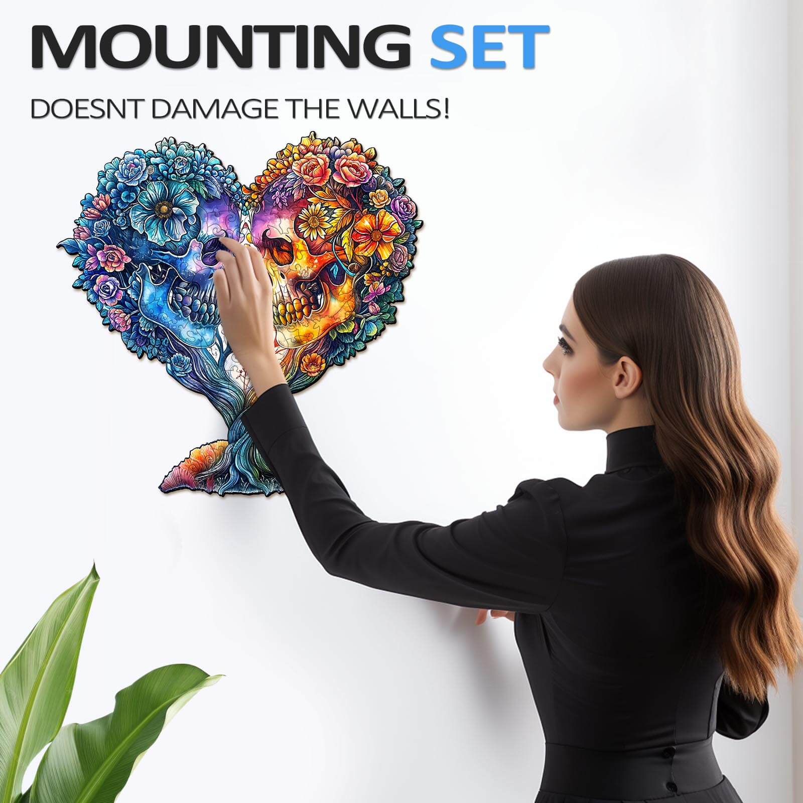 Woman applying Skull and Love jigsaw puzzle to wall with mounting set, showcasing vibrant artwork.