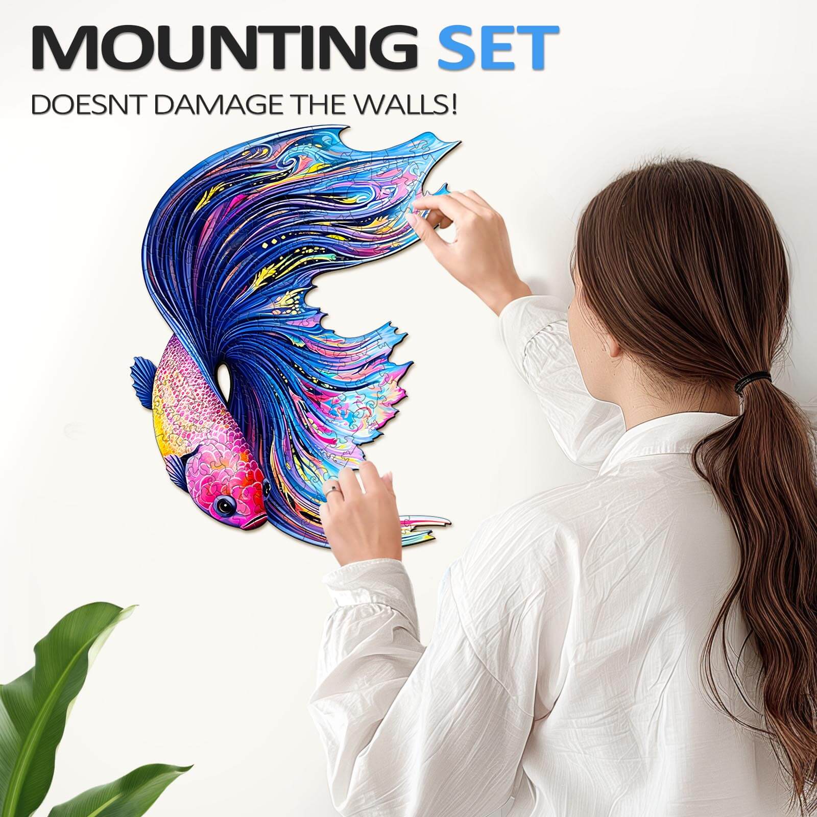 A woman attaching a colorful Half Moon Betta puzzle on the wall using a mounting set that doesn't damage the walls.