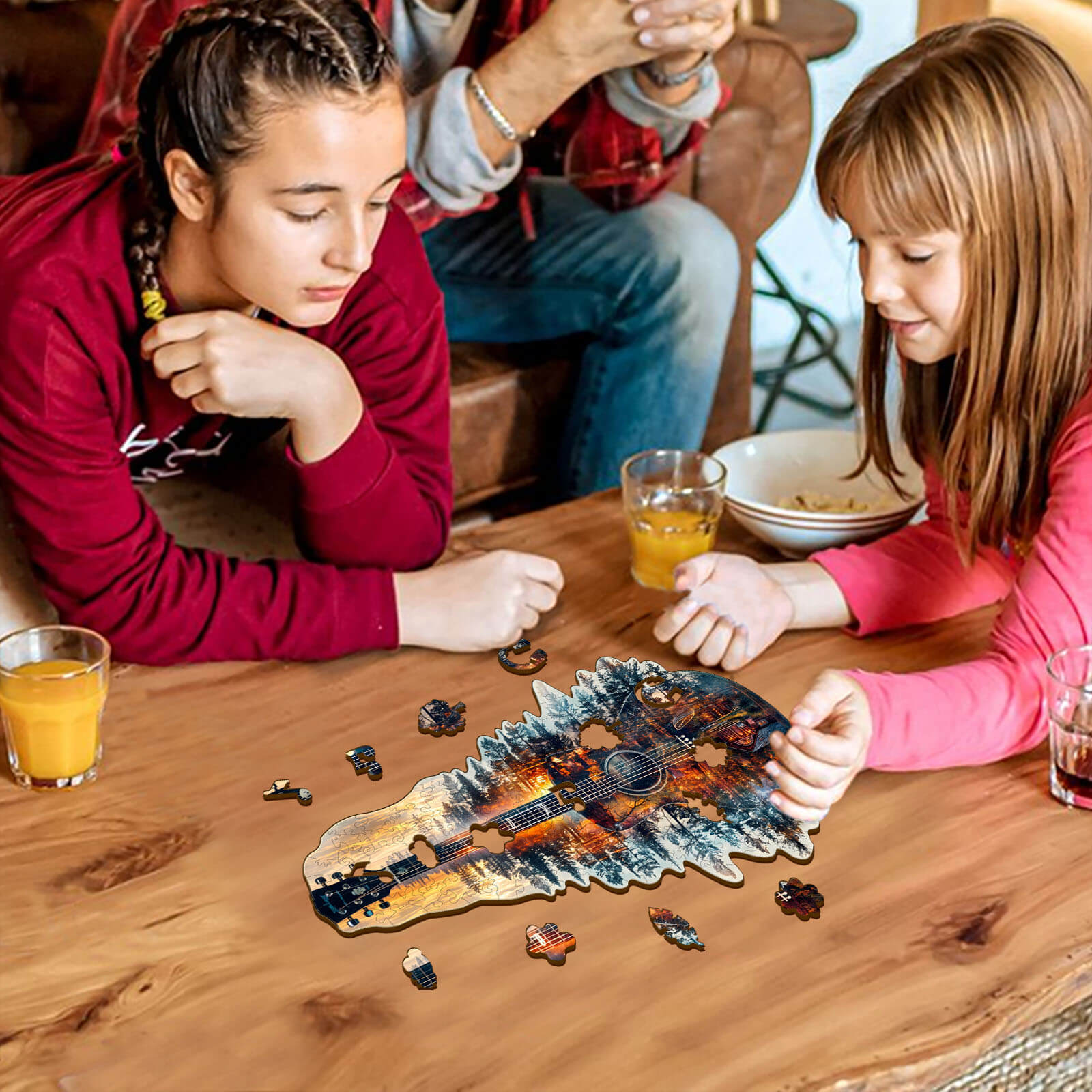 Two girls assembling a Sunset guitar wooden jigsaw puzzle on a wooden table with drinks around them.