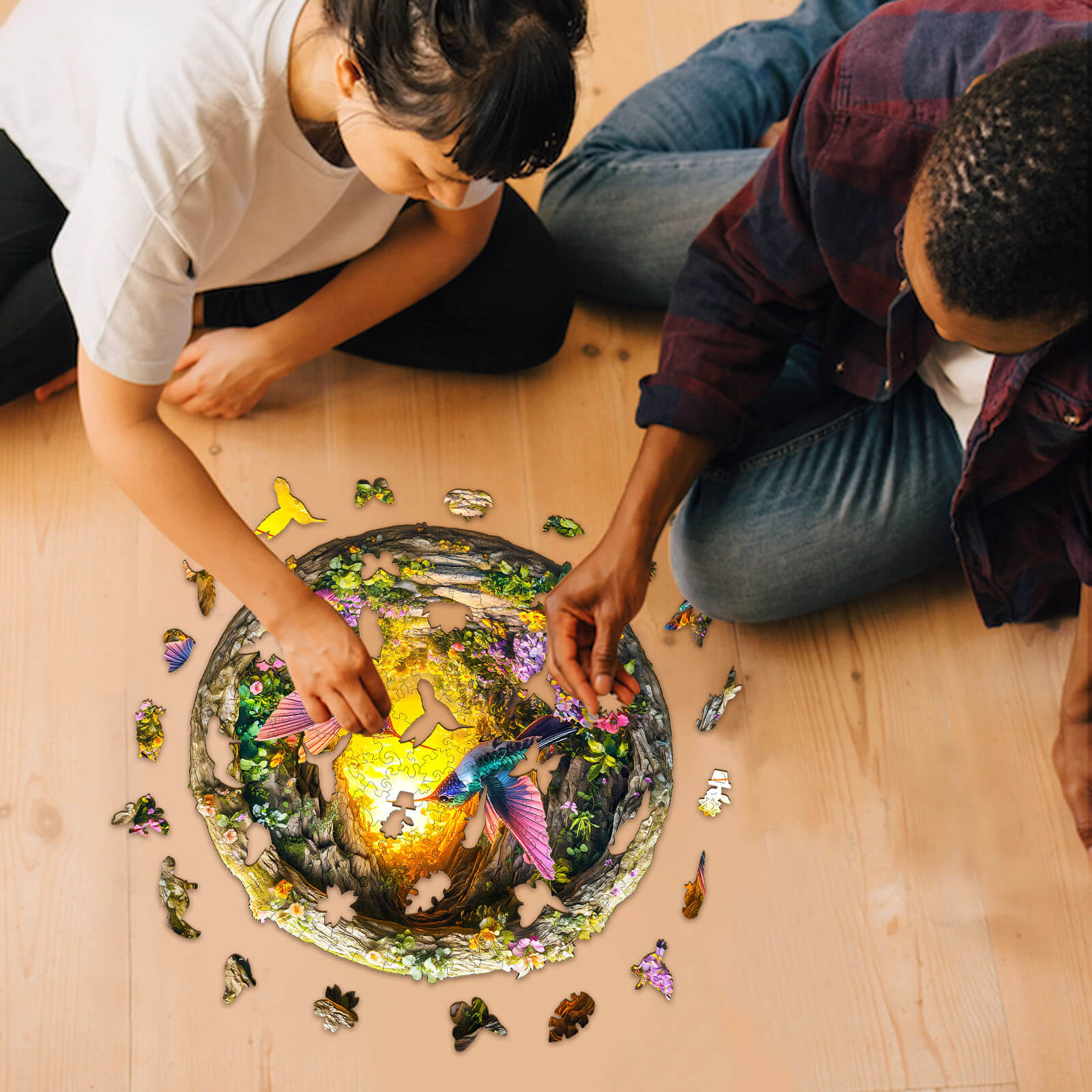 Two people assembling the 3D Hummingbird in the Cave-1 wooden jigsaw puzzle on a wooden floor.