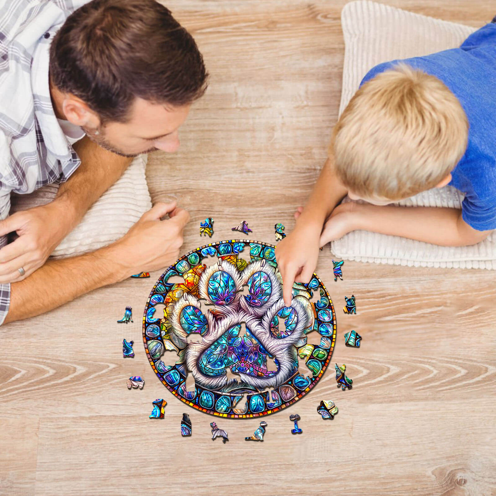 Father and son enjoying a colorful stained glass paw prints wooden jigsaw puzzle on a wooden floor.