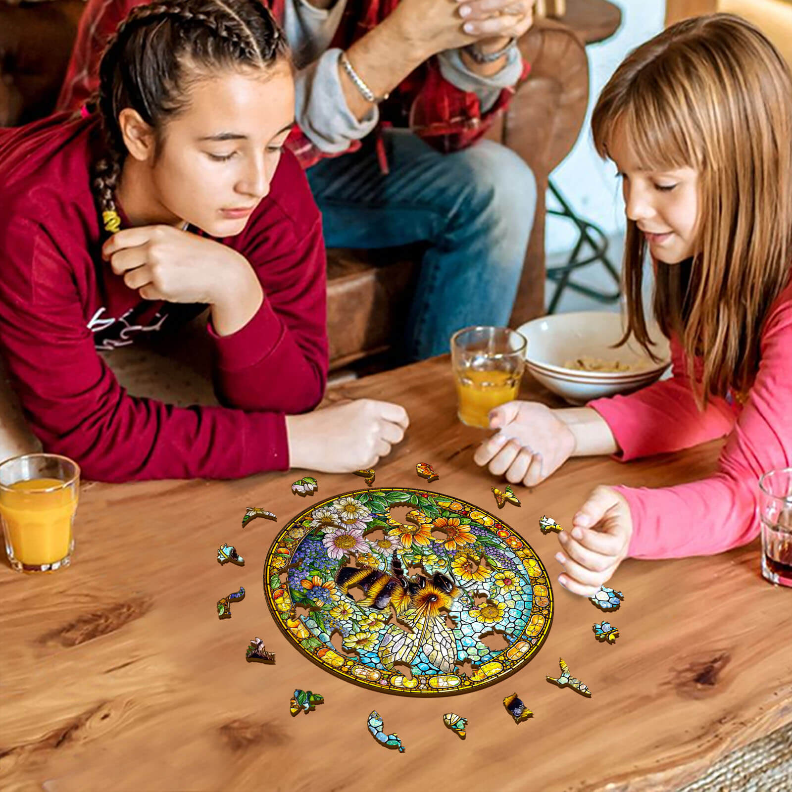 Two girls enjoying a Bee spring wooden jigsaw puzzle on a table, focusing on the colorful pieces and floral design.
