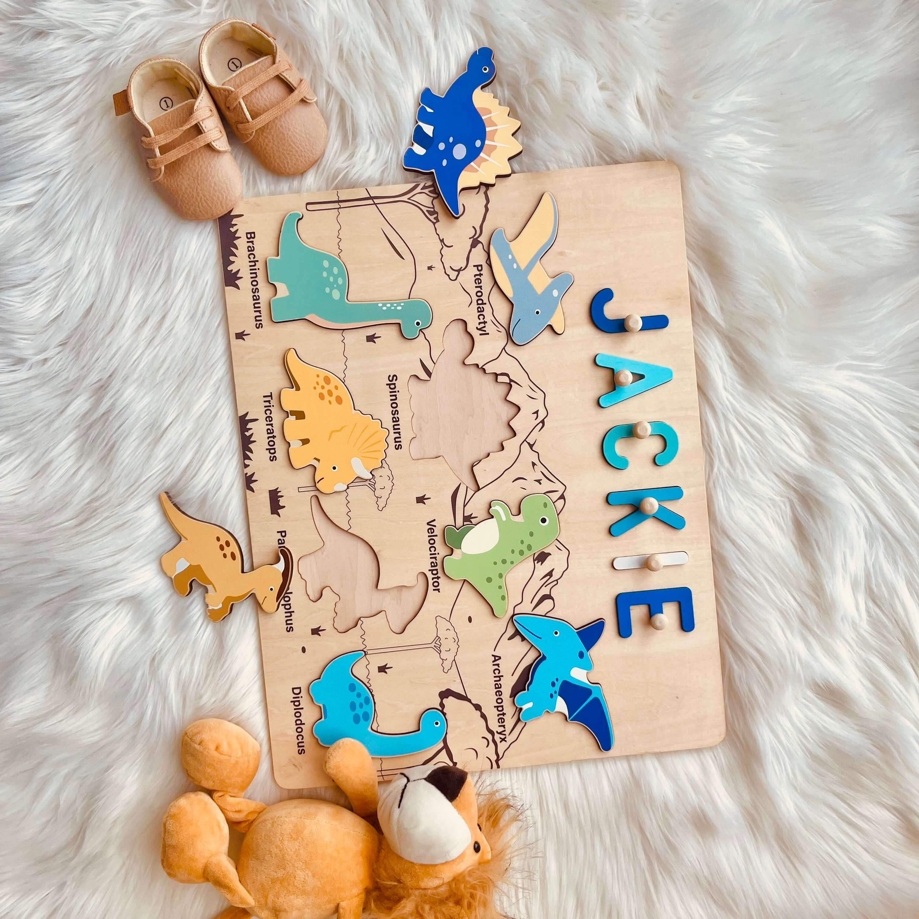 Personalized dinosaur name puzzle with colorful wooden dinosaur pieces and the name 'Jackie' on a soft surface.