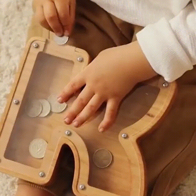 Child's hand placing coins into a personalized wooden letter piggy bank, promoting savings awareness.