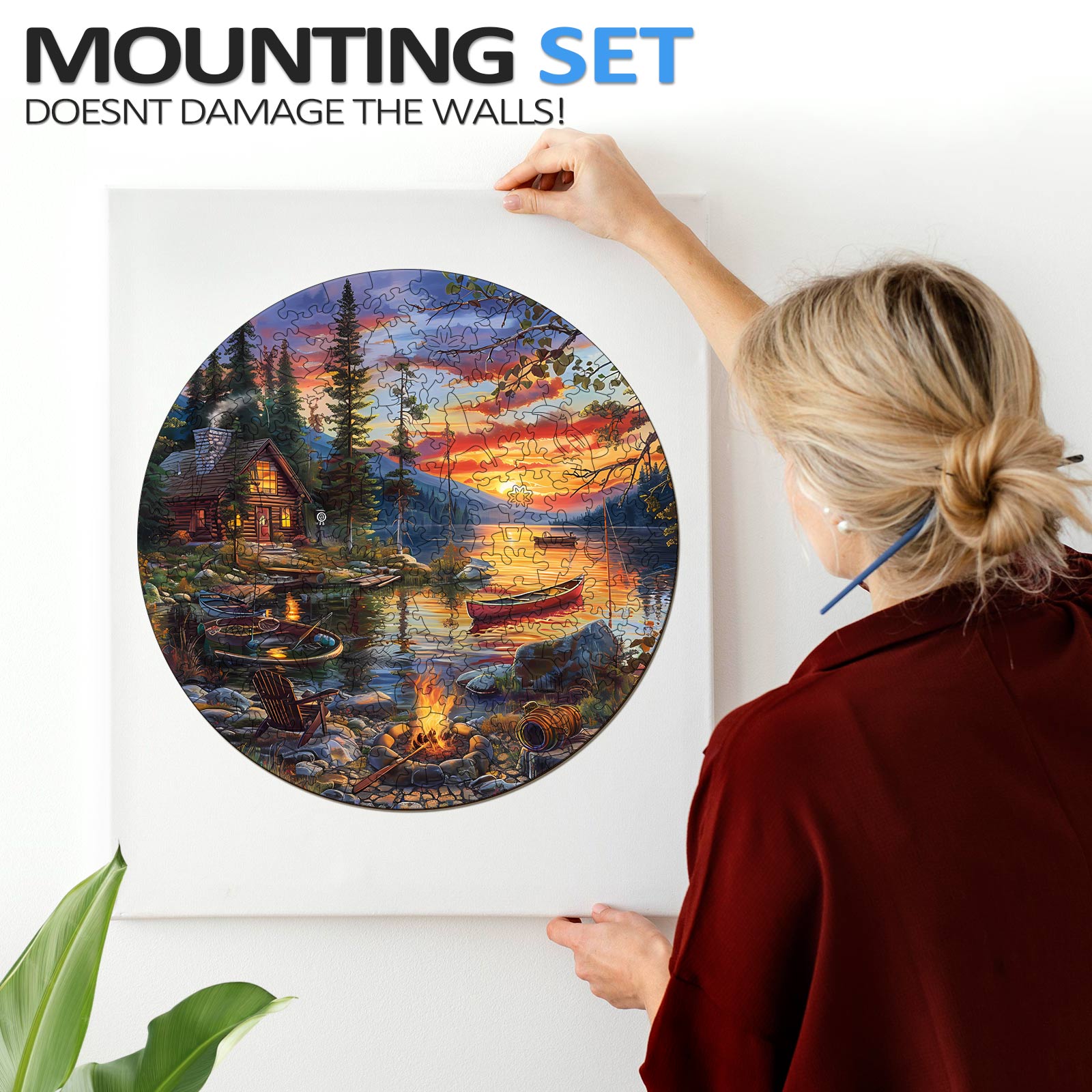 A woman hanging a round jigsaw puzzle of a serene lake sunset using a damage-free mounting set.