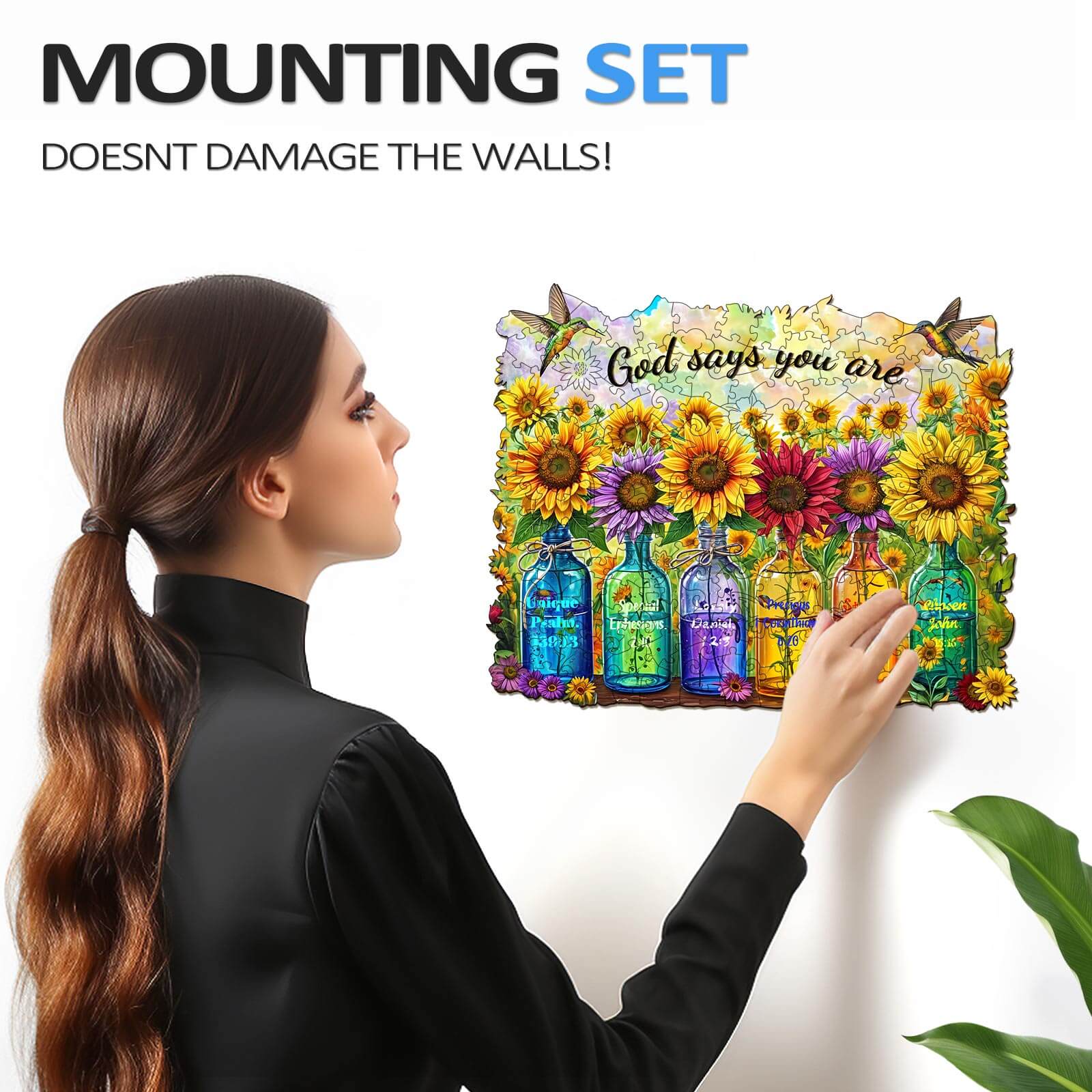Person using a mounting set to hang a colorful puzzle with sunflowers and the phrase 'God says you are' on the wall.