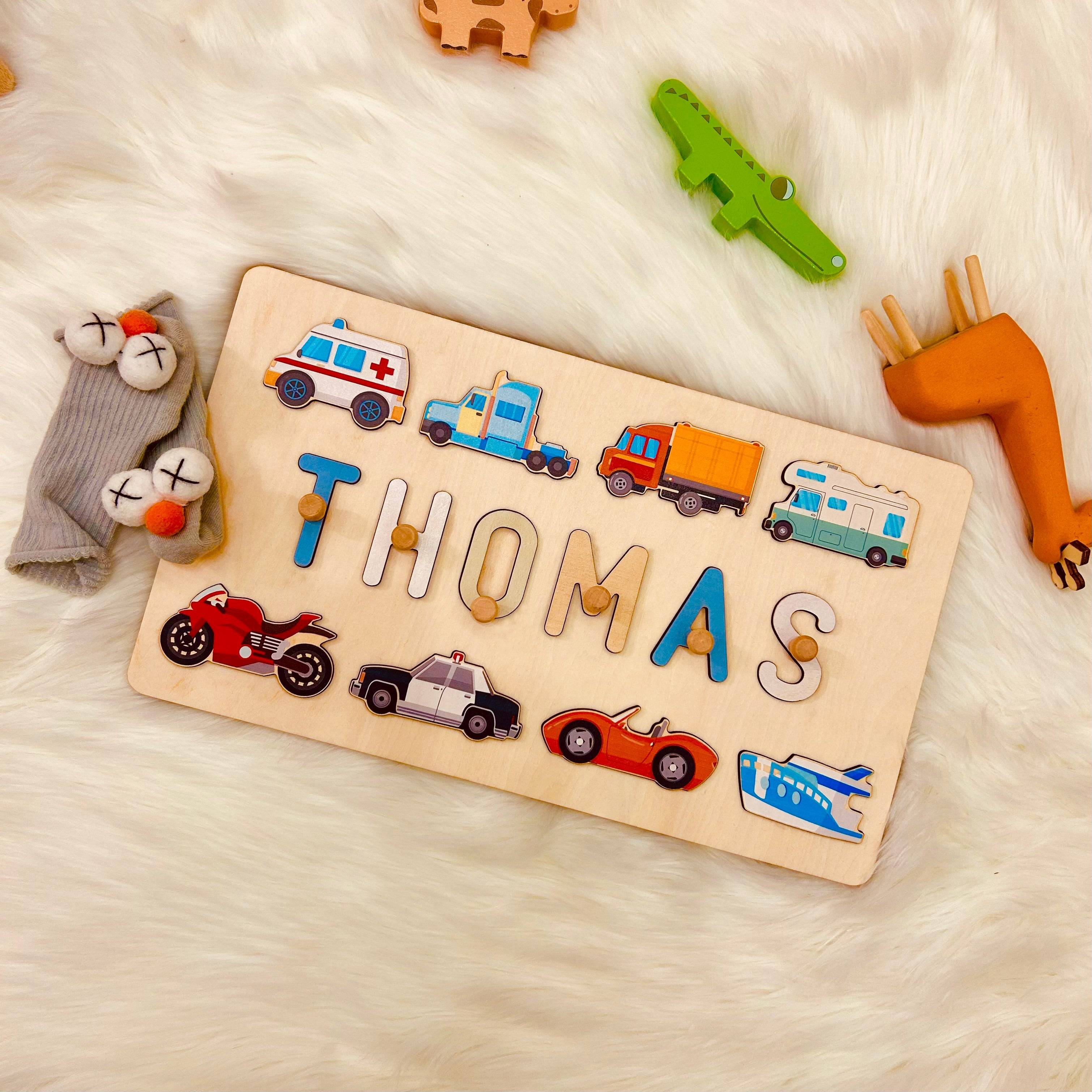Personalized wooden baby name puzzle with traffic-themed icons spelling 'THOMAS' on soft fur background.