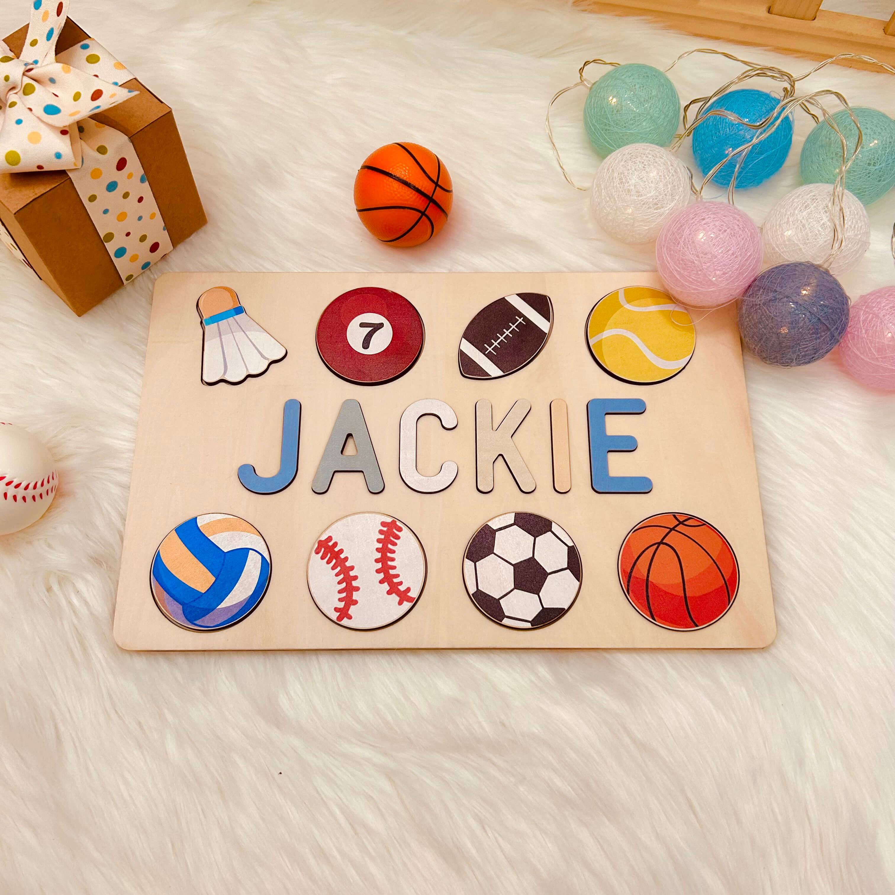 Personalized wooden baby name puzzle with sports icons, featuring the name 'JACKIE' and colorful balls.