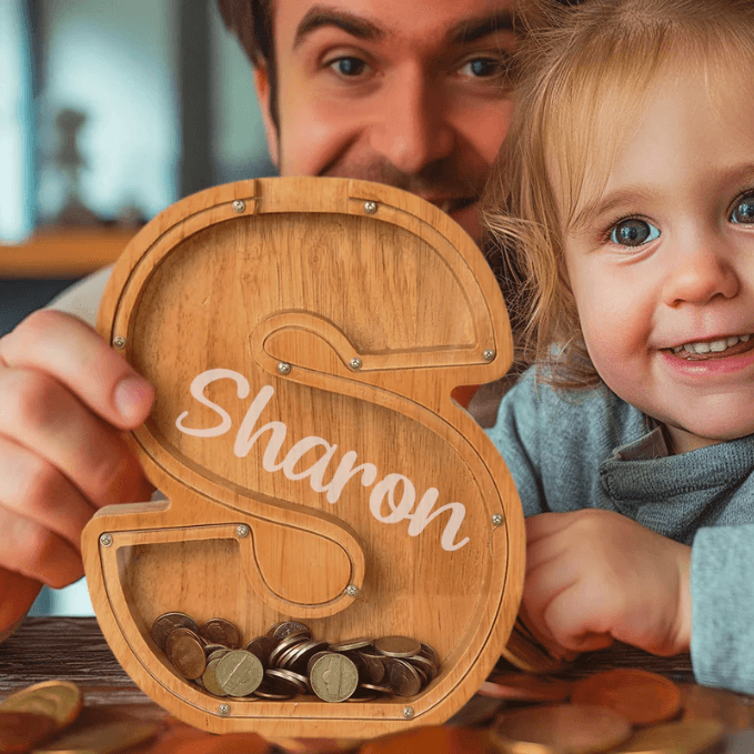 Child smiling with personalized wooden letter piggy bank, teaching the value of saving money.