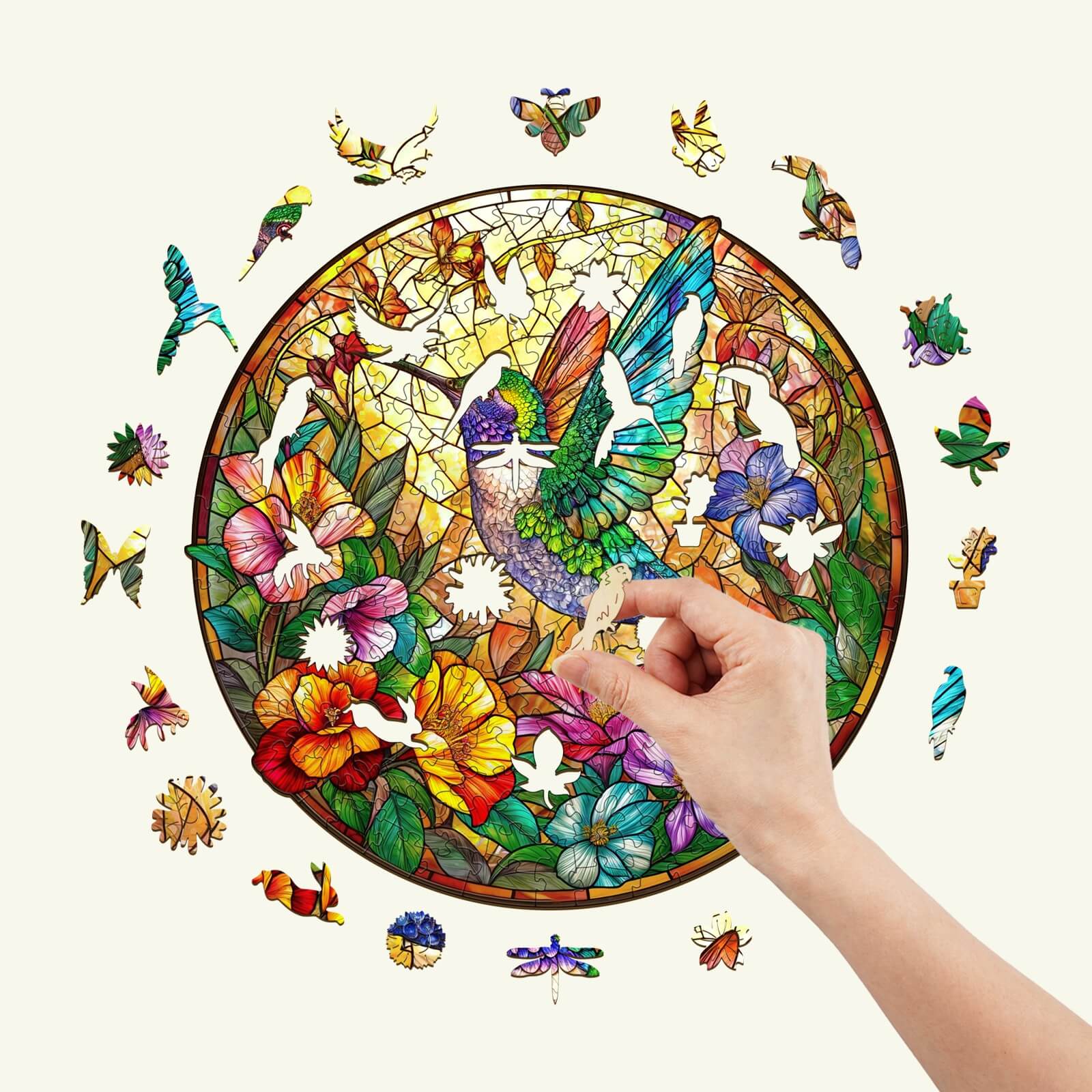 Hand placing a piece in the Stained Glass Hummingbird wooden jigsaw puzzle surrounded by colorful floral designs.