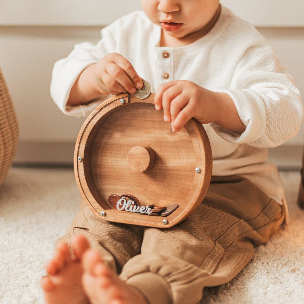 Child putting a coin in a personalized wooden letter piggy bank, promoting financial awareness and savings.