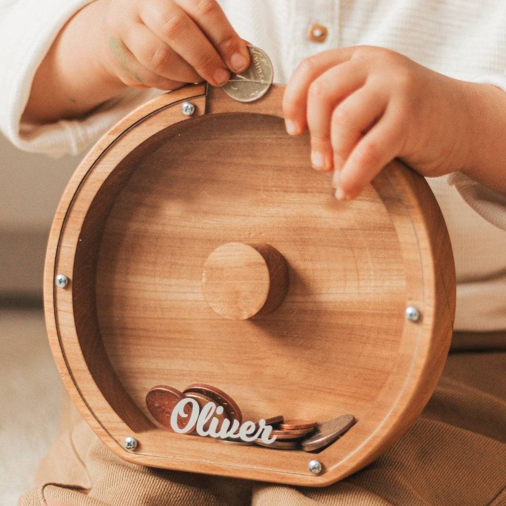 Child inserting a coin into a personalized wooden letter piggy bank named Oliver, promoting savings awareness.