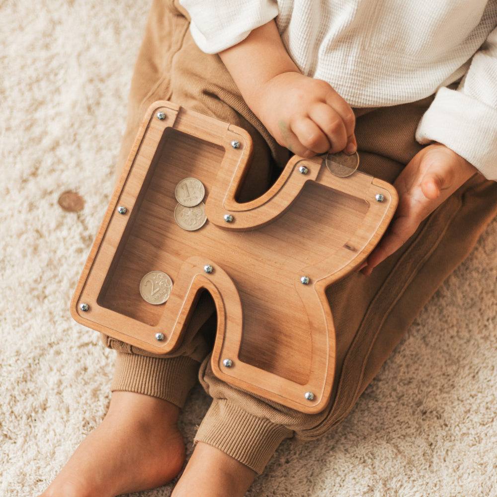Child holding a personalized wooden letter piggy bank designed for saving coins, promoting financial awareness.