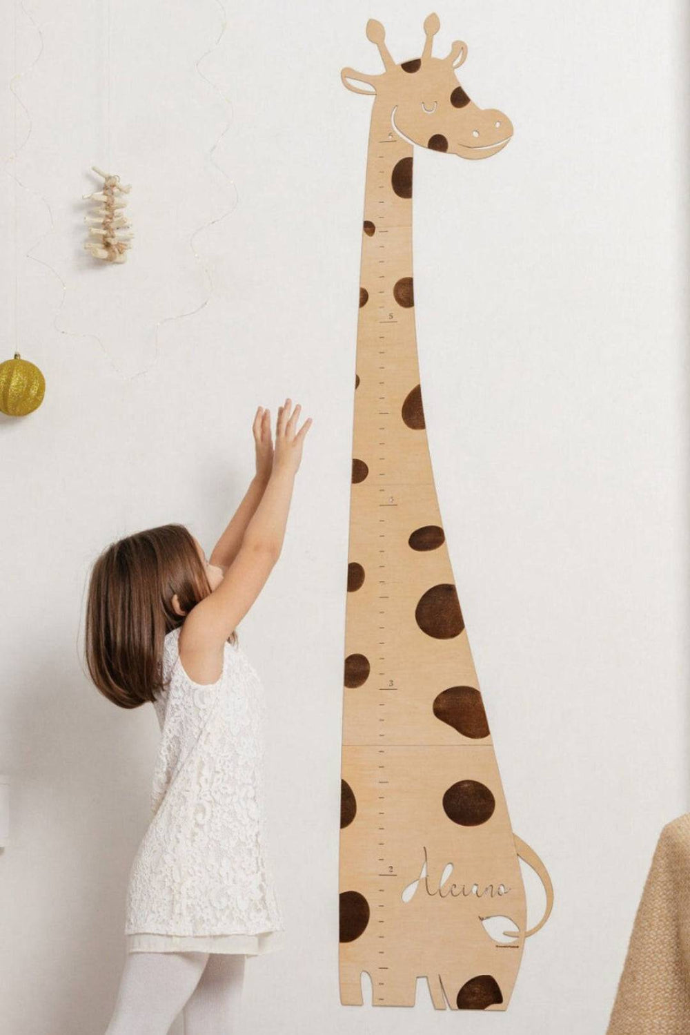 Child measuring height next to personalized wooden giraffe growth chart in nursery decor.