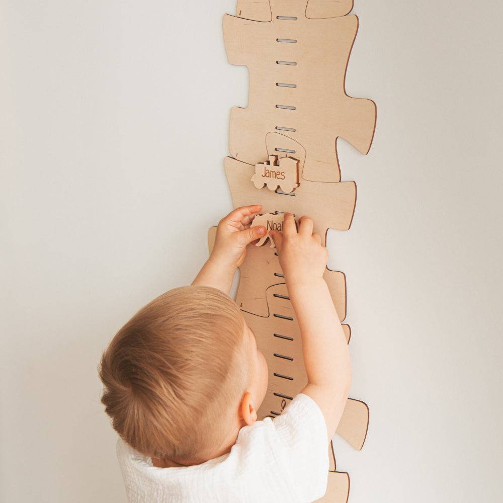 Child interacting with a personalized wooden growth chart, measuring height with custom markers attached.