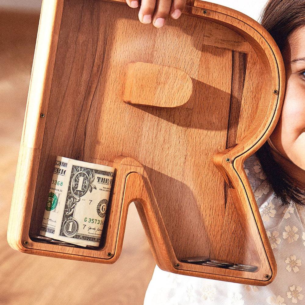 Personalized wooden letter piggy bank with dollar bills inside, perfect gift for kids to save money.