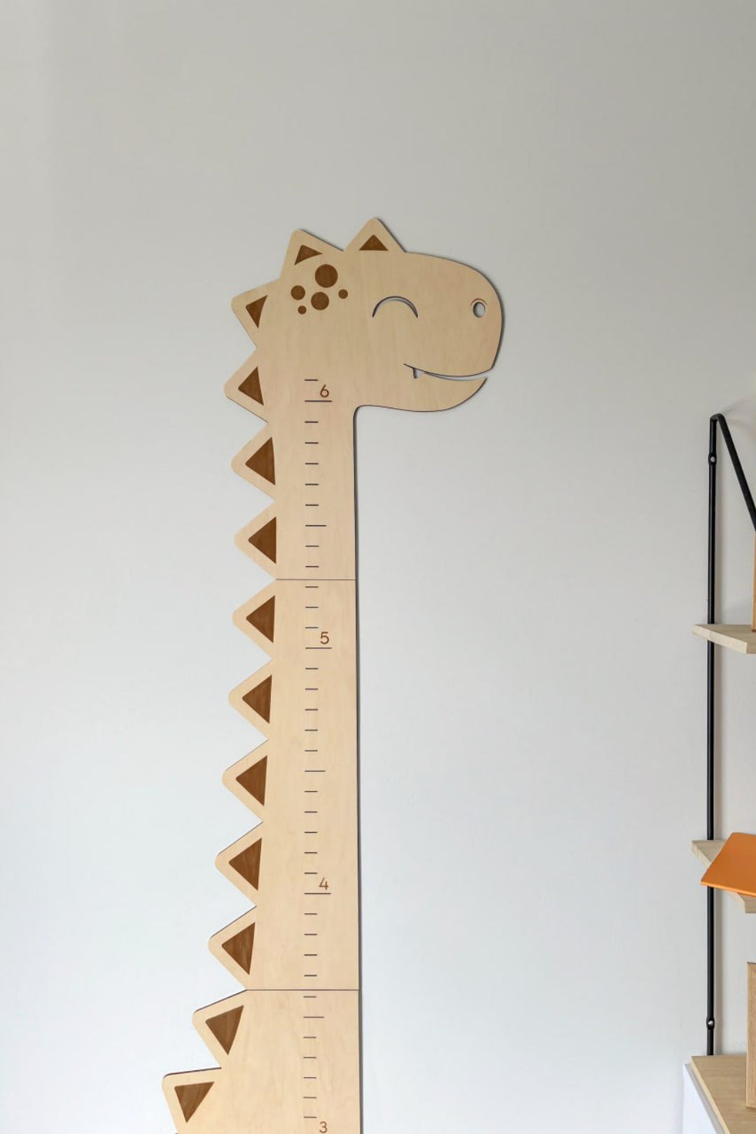Personalized wooden dinosaur growth chart ruler on a wall, featuring a cute dinosaur design and measurement marks.