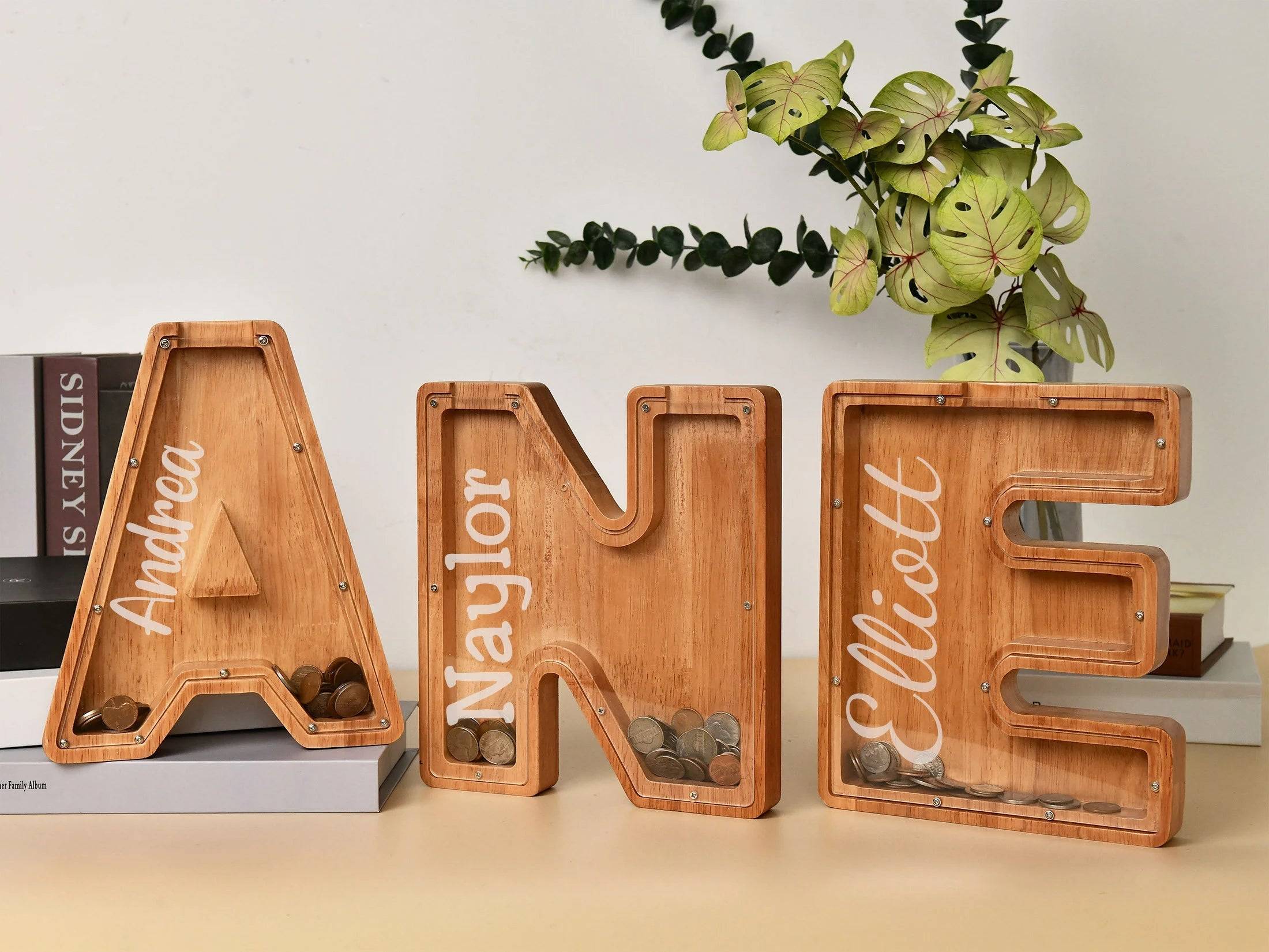 Personalized wooden letter piggy banks for kids, featuring names Andrea, Naylor, and Elliott, promoting financial literacy.