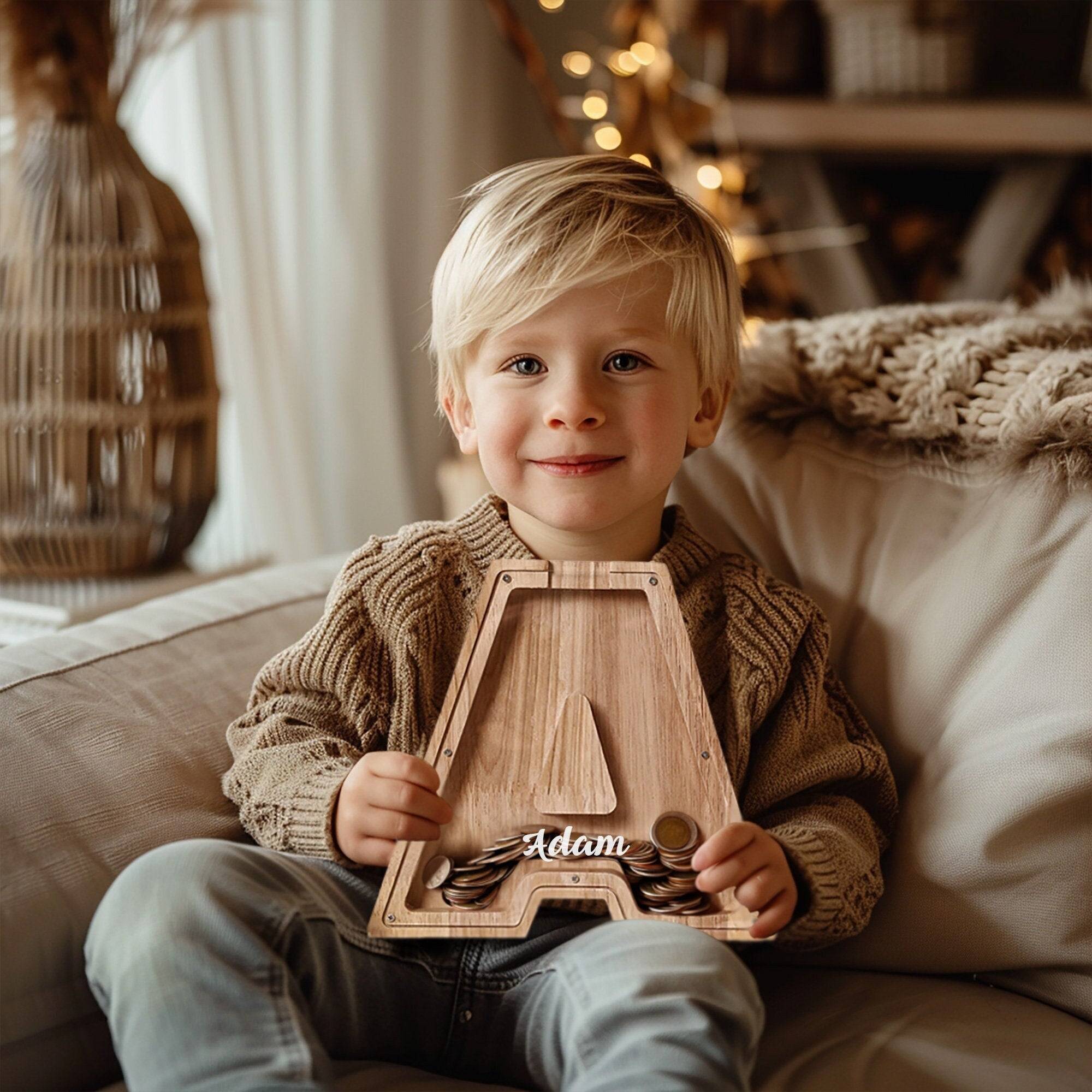 Smiling boy holding a personalized wooden letter piggy bank, promoting savings and financial awareness for kids.