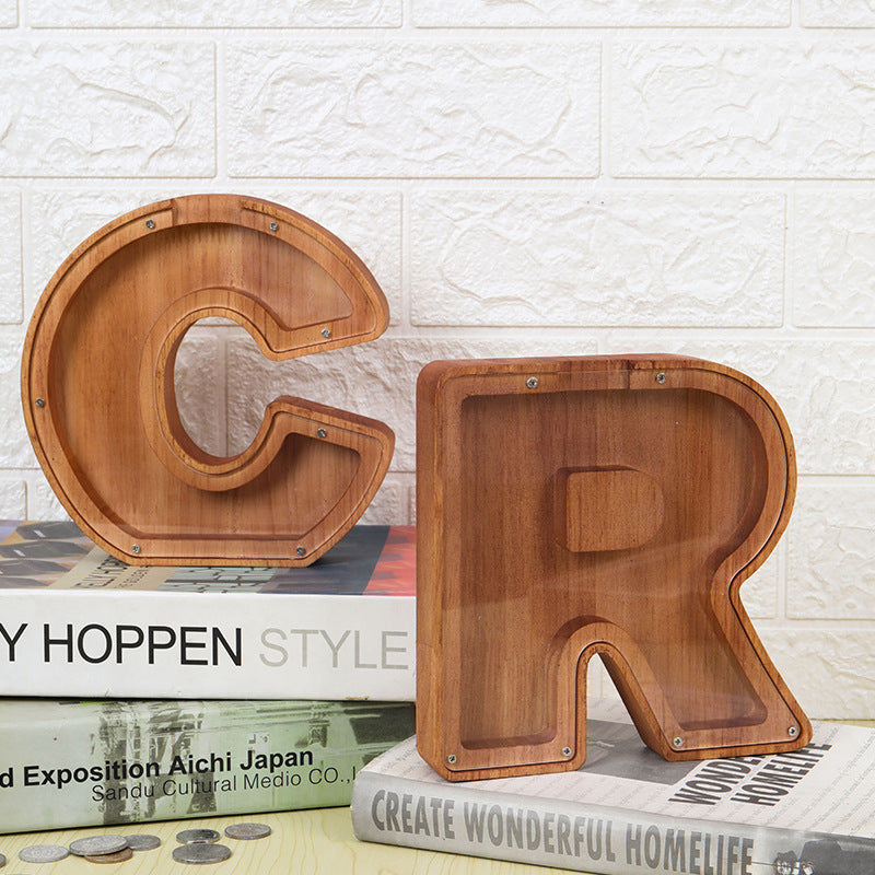 Personalized wooden letter piggy banks 'C' and 'R' on a stack of books, ideal custom gifts for kids' savings.